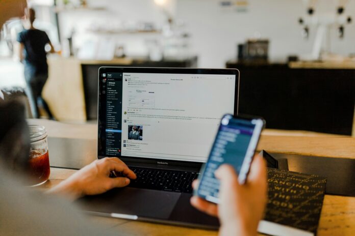 Image of a person sitting in front of their computer and looking at their phone.