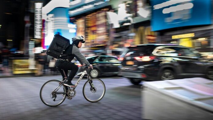 Image of an individual writing to deliver while on a bicycle in NYC.