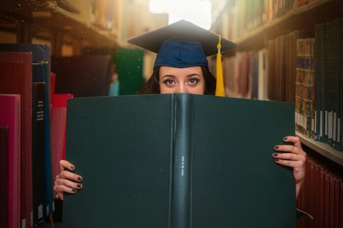 Image of a woman with a graduation cap holding a big book.