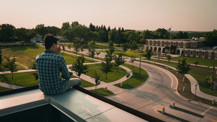 Image of an individual sitting on a building overlooking a college campus.