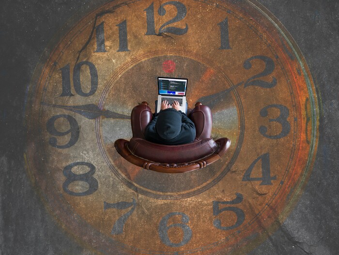 Image of an individual sitting on a couch with a laptop on top of a painting of a clock.